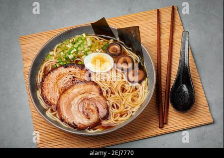Un Shoyu Ramen dans un bol gris sur une table en béton. Cuisine japonaise soupe de nouilles à la viande avec du chashu de porc. Cuisine asiatique Banque D'Images