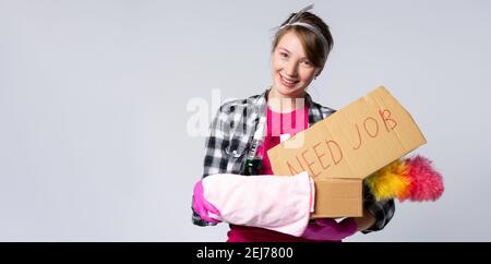 Portrait de la jeune femme de nettoyage pensive en tablier avec un panier avec des détergents et des brosses isolées sur blanc . Personnel de nettoyage expérimenté Banque D'Images