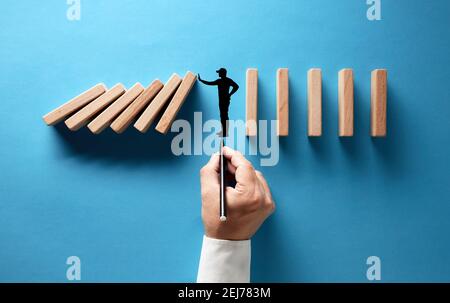 Homme d'affaires main dessin silhouette d'un homme faisant un geste d'arrêt pour empêcher les dominos en bois de s'effondrer sur fond bleu. Banque D'Images