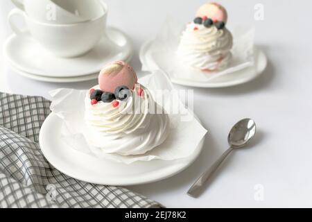 Encore vie Pavlova gâteau meringue décoré macaron sur fond blanc. Tasses à thé et serviette sur table en bois Banque D'Images