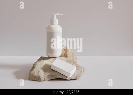 Collection de produits cosmétiques sur fond beige. Bouteille de pompe en plastique blanc pour shampooing, maquette de lotion sur podium en pierre. Boîte de papier à savon vierge Banque D'Images