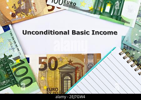 Photo TopView sur le thème du revenu de base universel. Les mots revenu de base inconditionnel sur papier, entourés de billets en euros et d'un bloc-notes Banque D'Images