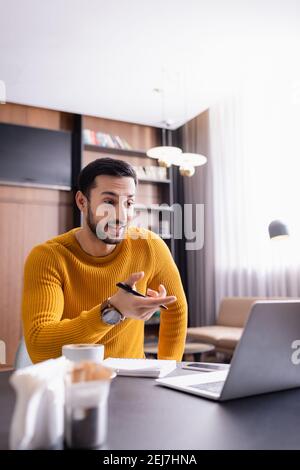 un pigiste arabe étonnant pointant vers un ordinateur portable dans un restaurant, avant-plan flou Banque D'Images