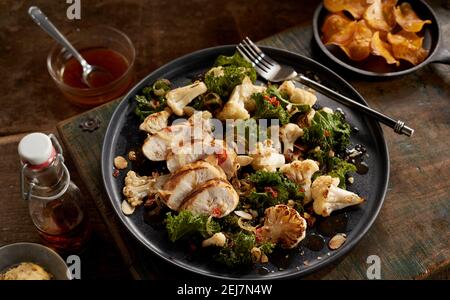 Du dessus du poulet avec chou-fleur poêlé et chou-fleur servi sur l'assiette sur la table en bois rustique près d'une bouteille de vinaigre et pommes de terre frites au chili sauc Banque D'Images