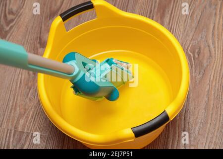 Balai bleu avec lavabo jaune pour nettoyer les sols. Nettoyage d'un parquet sous un arbre. Banque D'Images