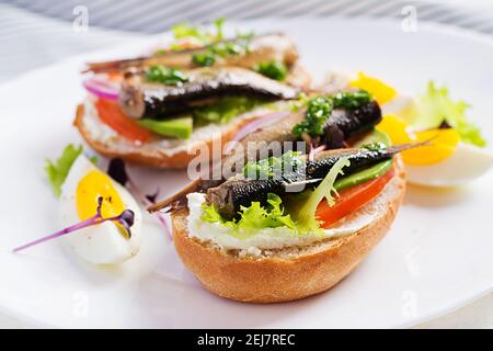 Sandwich - smorrebrod avec des sparats, de l'avocat, des tomates, des œufs et du fromage à la crème sur une assiette blanche. Cuisine danoise. Concept écologique. Banque D'Images