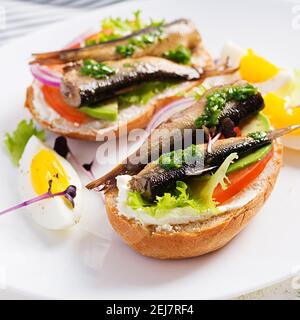 Sandwich - smorrebrod avec des sparats, de l'avocat, des tomates, des œufs et du fromage à la crème sur une assiette blanche. Cuisine danoise. Concept écologique. Banque D'Images