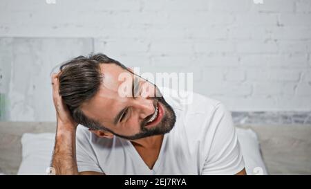 un homme à barbe heureux se touchant la tête dans la chambre le matin Banque D'Images