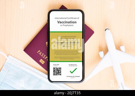 Un masque facial, un avion modèle, un passeport et un smartphone avec un certificat de vaccination contre la maladie de Covid-19 sont disposés sur une table en bois. Banque D'Images