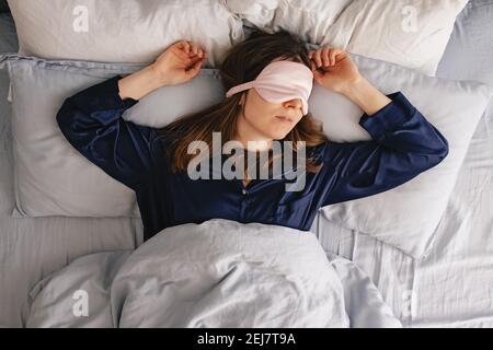 Une jeune femme en soie dors-bien dormant dans un lit avec les yeux couverts de masque. Banque D'Images