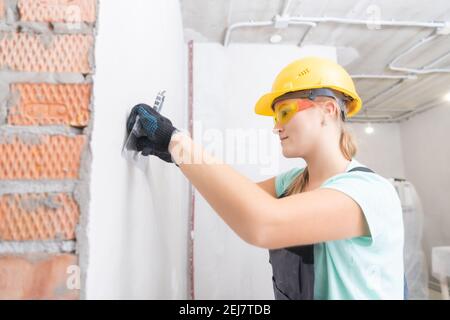 Nettoyage d'un mur en béton contre les défauts, réparation et construction, préparation de la surface à l'aide d'une spatule avant application du plâtre. Banque D'Images
