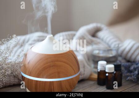 Diffuseur d'huile aromatique moderne sur surface en bois avec élément tricoté, eau et huiles en pots. Banque D'Images