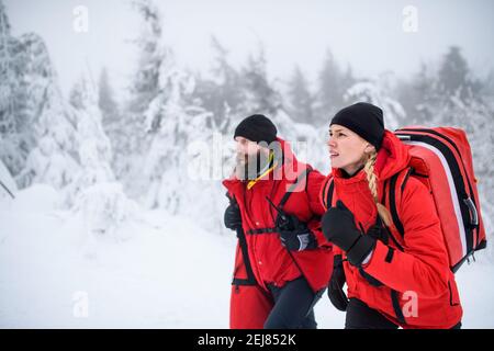 Ambulanciers paramédicaux du service de sauvetage en montagne marchant à l'extérieur en hiver dans la forêt. Banque D'Images