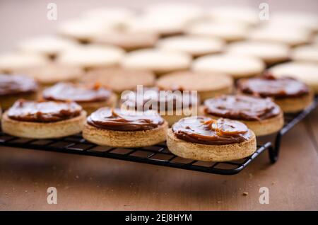 Biscuits à l'alfajor à la fécule de maïs avec caramel au lait sur un support noir et sur fond de bois. Banque D'Images