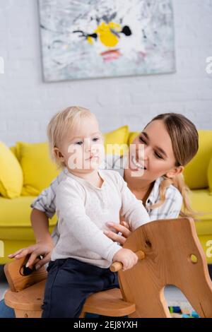 bonne jeune femme près d'un tout-petit garçon à cheval à bascule accueil Banque D'Images