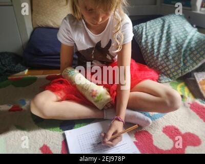 Fille européenne de 7-9 ans avec un bras cassé plâtré faisant ses devoirs avec sa main gauche, France. Banque D'Images