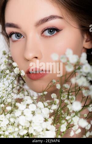 Jeune femme regardant l'appareil photo près de petites fleurs blanches sur premier plan flou sur fond blanc Banque D'Images