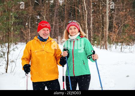 Couple senior marchant avec des bâtons de marche nordiques en hiver enneigé stationnement Banque D'Images