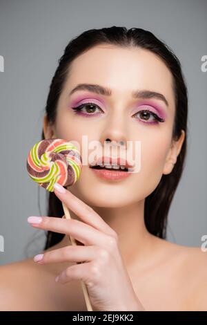 jeune femme avec des ombres à paupières roses tenant la lollipop isolé dessus gris Banque D'Images