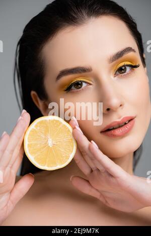 brunette jeune femme tenant la moitié de citron juteux isolé dessus gris Banque D'Images