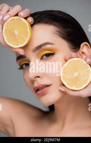 jeune femme brune tenant des moitiés de citron jaune isolées sur le gris Banque D'Images