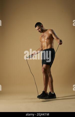 Portrait de l'adorable sportif caucasien dans le noir sportswear tenant un saut corde dans les mains en se tenant dans le studio isolé sur arrière-plan jaune Banque D'Images