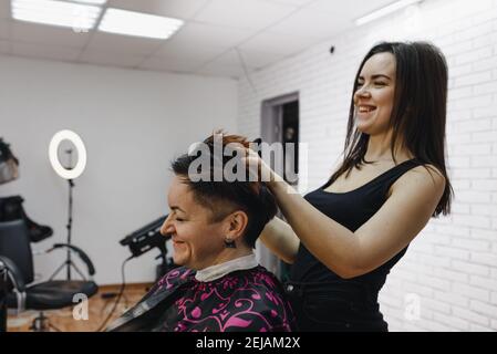 une coiffeuse de fille fait ses cheveux pour une cliente dans un salon de beauté moderne et rie avec rire ensemble. Banque D'Images