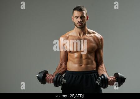 Portrait à la taille du sportif caucasien fort et barbu poids de levage de vêtements de sport noirs dans la pièce à l'intérieur Banque D'Images