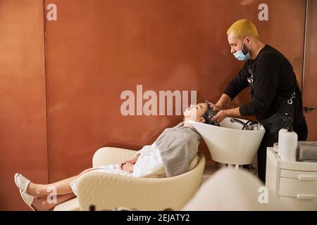 Une femme s'est couchée dans la chaise pendant la procédure de shampooing Banque D'Images