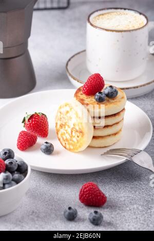 Crêpes au fromage cottage avec baies fraîches, une tasse de café et une cafetière sur une table en pierre. Délicieux petit déjeuner. Photo verticale - image Banque D'Images