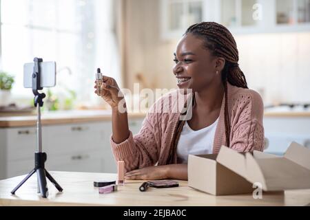 Blogging de beauté. Femme noire souriante examinant les produits de maquillage à l'avant de l'appareil photo Banque D'Images