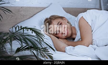 jeune femme joyeuse regardant l'appareil photo tout en étant couché dans le lit sur un premier plan flou Banque D'Images