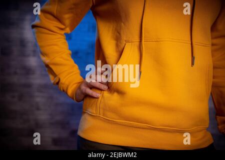 Vue avant de la partie du corps de la jeune femme en sweat-shirt. Gros plan de la figure d'une femme méconnaissable avec sa main sur le côté du bac en brique grise Banque D'Images