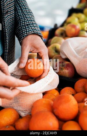 gros plan d'un jeune homme caucasien utilisant un sac en maille textile réutilisable pour acheter des mandarines à un greengrocer ou à un marché de rue, comme mesure de réduire Banque D'Images