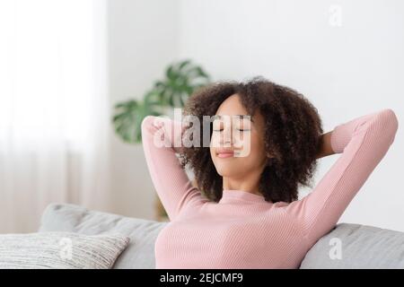 Une femme heureuse se détendant sur un canapé confortable, appréciant du temps libre à la maison, agréable matin tranquille, rêvant et planifiant la journée Banque D'Images