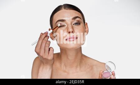 Jeune femme adulte appliquant une ombre oculaire avec une brosse cosmétique isolée sur blanc Banque D'Images