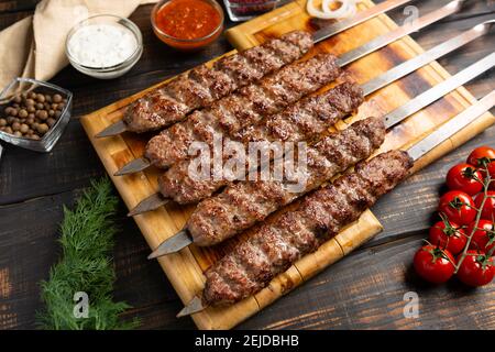 kebab fait de viande hachée sur brochette de métal avec légumes et sauce sur fond de bois sombre Banque D'Images