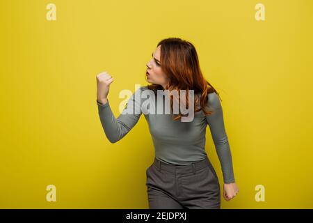 femme en colère avec des cheveux bouclés montrant le poing fermé sur le jaune Banque D'Images