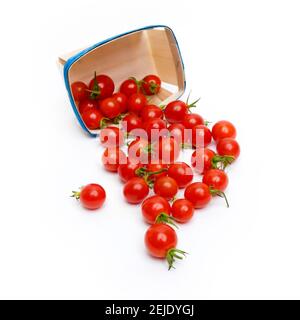 Les tomates cerises fraîches débordent d'un récipient bleu sur un fond blanc lors d'une séance de préparation de la cuisine Banque D'Images