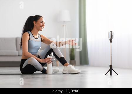 Belle femme assise sur un tapis de yoga, ayant un appel vidéo Banque D'Images