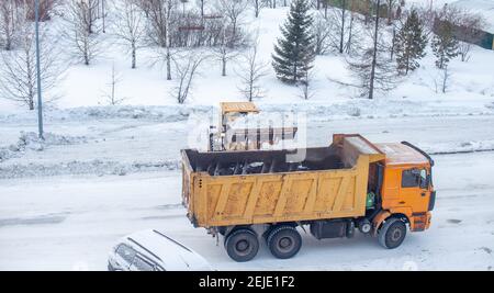 Le gros tracteur jaune nettoie la neige de la route et la charge dans le camion. Nettoyage et nettoyage des routes de la ville de la neige en hiver Banque D'Images