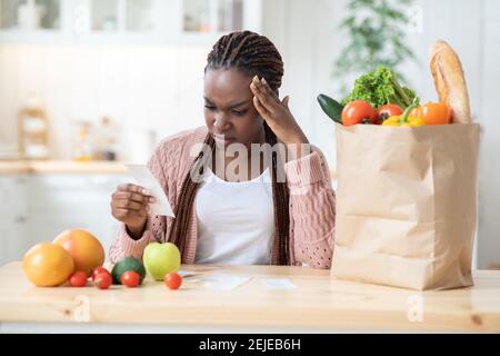 Dépenses d'épicerie. Inquiète Black Lady vérifier la facture dans la cuisine après les achats de nourriture Banque D'Images