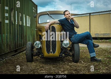 Ford populaire 1958 Hot Rod . jeune homme en Jean assis sur sa voiture et fumer . Banque D'Images