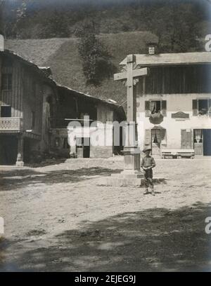 Photographie ancienne c1900, centre-ville rural européen, avec statue de croix et jeune garçon. Lieu exact inconnu, éventuellement Italie, France ou Suisse. SOURCE : PHOTO ORIGINALE Banque D'Images