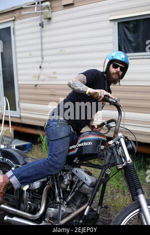 Un jeune homme se démontant d'une moto Harley Davidson portant un casque avec motif étoiles et rayures Banque D'Images