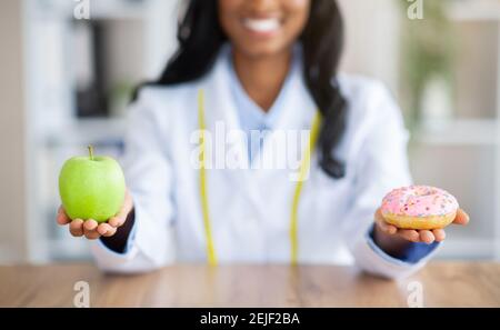 Vue en gros plan des mains du diététicien tenant la pomme fraîche et le donut à la table dans le bureau médical. Concept de régime Banque D'Images