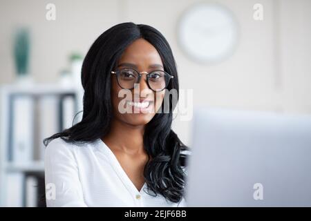 Portrait d'une femme d'affaires noire réussie souriant à l'appareil photo, travaillant avec un ordinateur portable dans un bureau moderne Banque D'Images