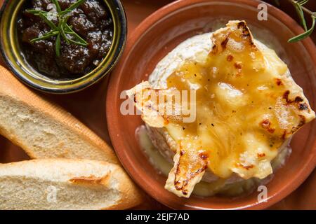 Camembert français qui a été cuit au four avec une sauce à la truffe, à l'ail et au miel, servi avec du pain français grillé et un chutney d'oignon caramélisé Banque D'Images