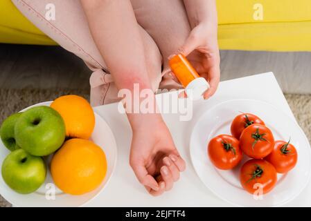 Vue rognée de la femme avec des pilules antiallergiques près de frais fruits et tomates Banque D'Images