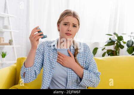 Femme mécontent de la réaction allergique en tenant l'inhalateur sur le canapé Banque D'Images